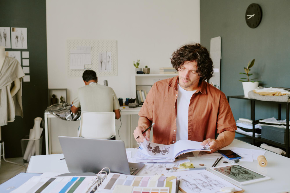 A designer working at a studio desk, a colleague behind them